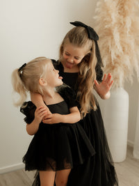 Gabrielle full length black flower girl dress and Gabrielle black toddler romper are worn by sisters. They also wear matching black tulle bows in their hair.