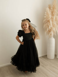 Gabrielle black flower girl dress and matching black large tulle bow are worn by a young girl.