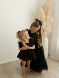 Sisters wearing matching black flower girl outfits, our Gabrielle black baby romper and Gabrielle black tulle girls dress.