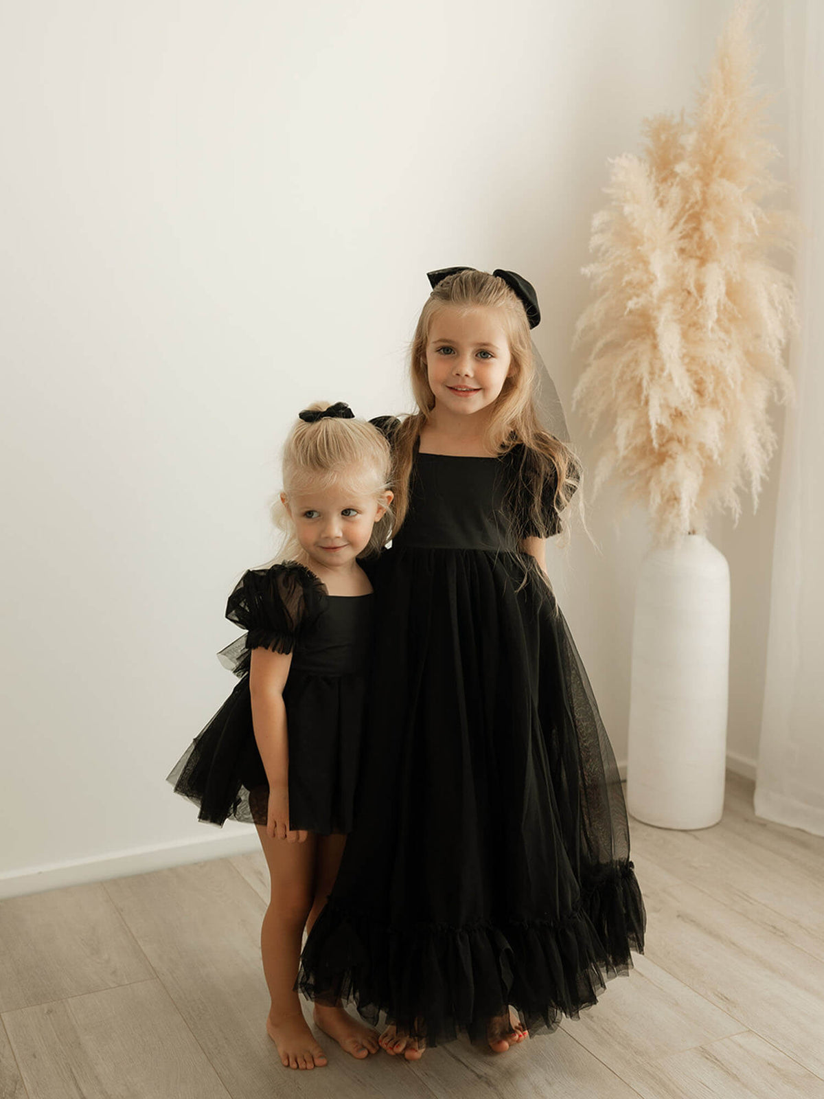 Black full length flower girl dress and black baby romper are worn by two sisters.