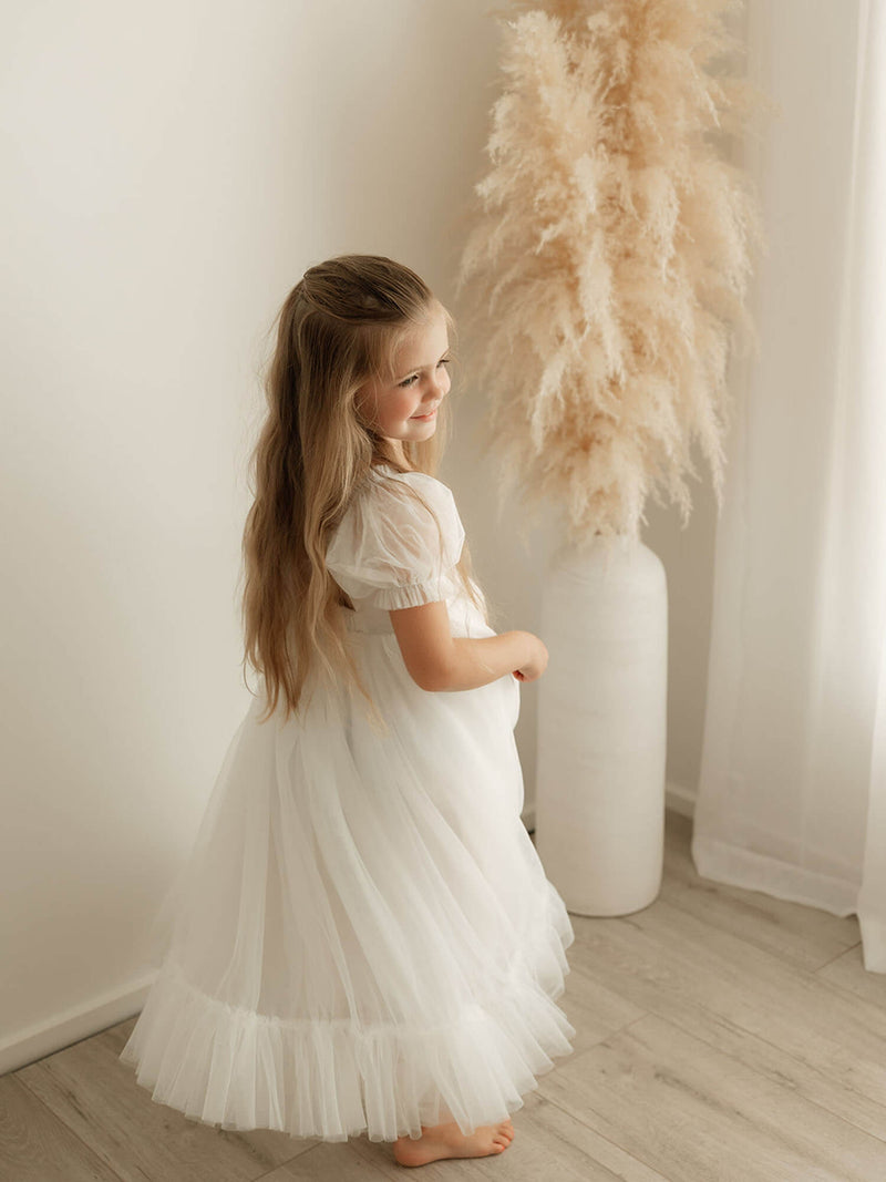 Gabrielle ivory tulle flower girl dress in full length is worn by a young girl, showing the tulle puff sleeves.