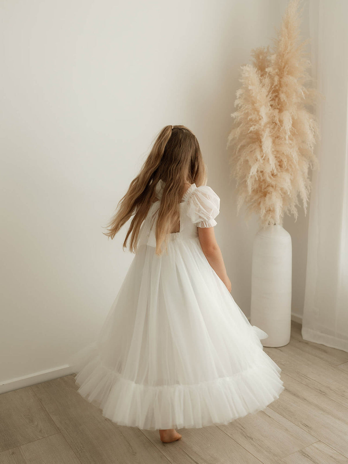 A young girl twirls wearing our Gabrielle ivory full length flower girl dress, showing the tulle bow detail at the back.