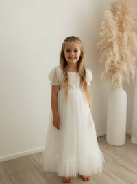 A young girl smiles wearing our full length Gabrielle flower girl dress in ivory.