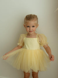 Gabrielle lemon yellow baby flower girl dress with tulle puff sleeves is worn by a young girl.