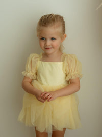 Young girl wearing a yellow tulle flower girl dress for babies and toddlers, against a plain background.