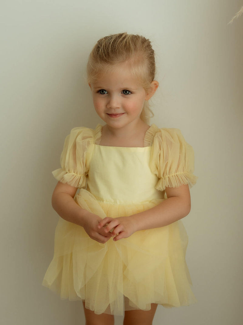 Young girl wearing a yellow tulle flower girl dress for babies and toddlers, against a plain background.