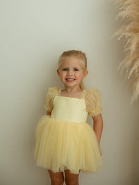 Young girl in a yellow party dress standing against a plain background.