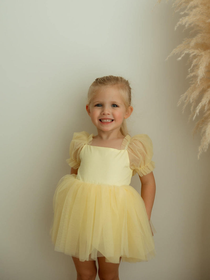 Young girl in a yellow party dress standing against a plain background.