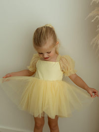 Gabrielle lemon flower girl romper is worn by a little girl, along with a matching lemon tulle bow hair clip.
