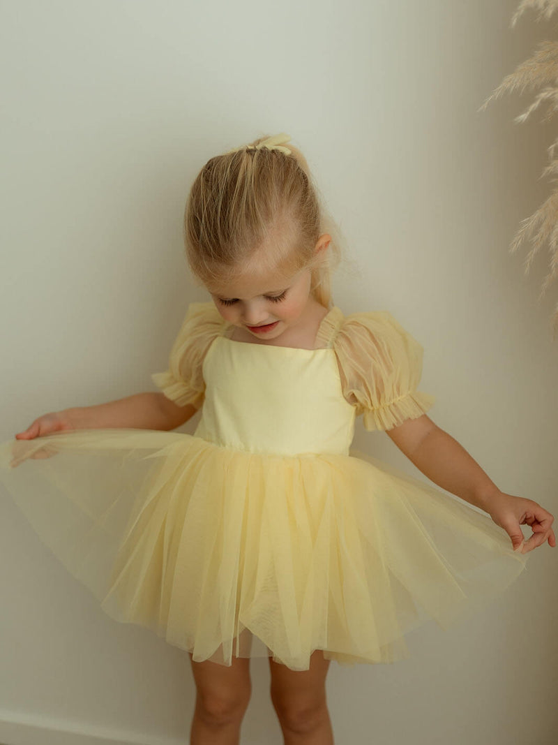 Gabrielle lemon flower girl romper is worn by a little girl, along with a matching lemon tulle bow hair clip.