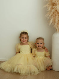Sisters sit smiling, wearing matching lemon flower girl dresses.