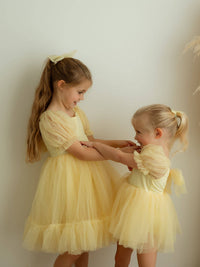 Sisters playing wearing matching lemon yellow flower girl dresses with tulle bows.