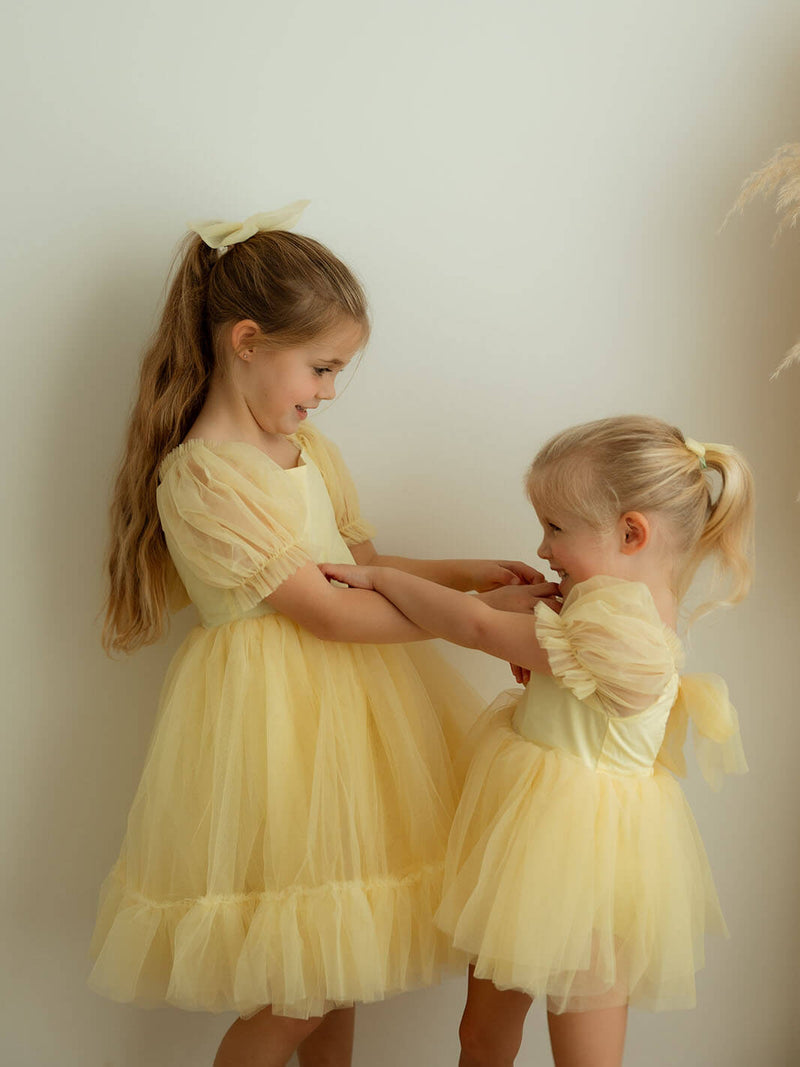 Sisters playing wearing matching lemon yellow flower girl dresses with tulle bows.