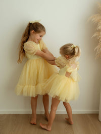 Sisters playing wearing matching lemon yellow flower girl outfits with yellow tulle bows.