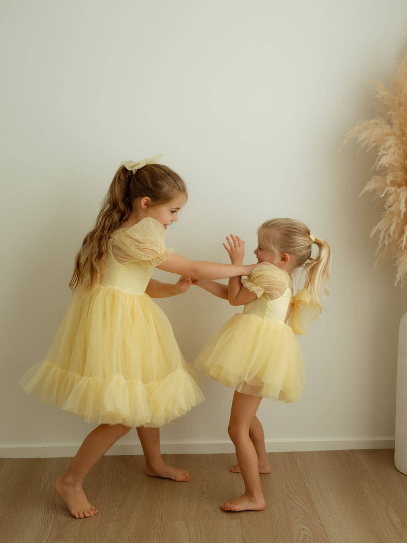 Two young girls playing in yellow tulle dresses with matching yellow tulle hair bows.