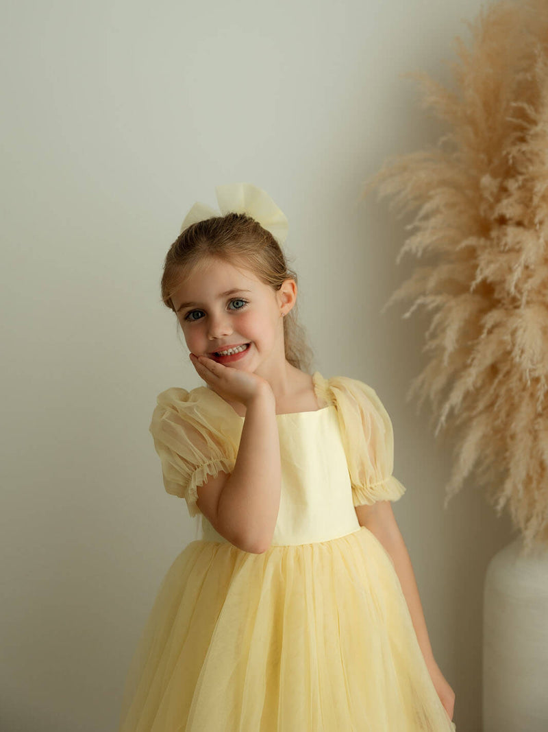 A little girl smiling wearing our Gabrielle lemon flower girl dress and a matching lemon tulle bow hair clip.