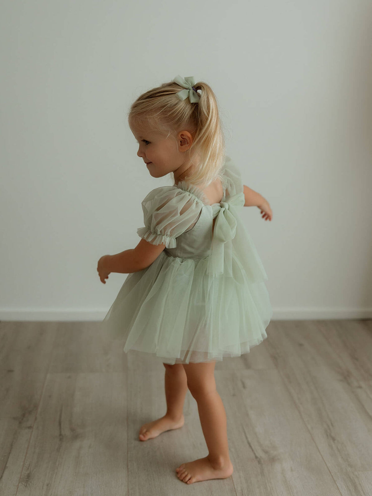 A toddler twirls wearing our Gabrielle sage green baby flower girl romper and matching pigtail bows.