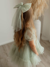A young girl wears our sage tulle bow hair clip in large, along with our Gabrielle sage flower girl dress.