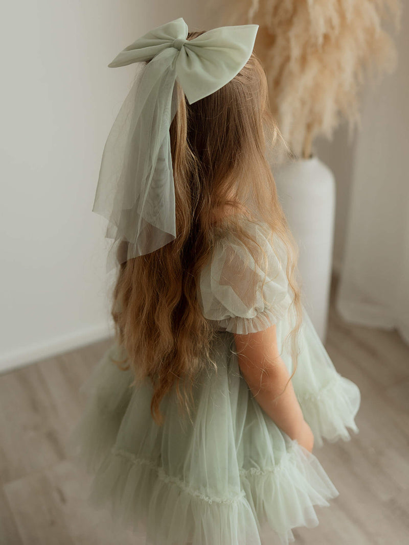 A young girl wears our sage tulle bow hair clip in large, along with our Gabrielle sage flower girl dress.
