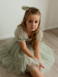 Sage green tulle flower girl dress, our Gabrielle dress, is worn by a young girl who sits on the floor.