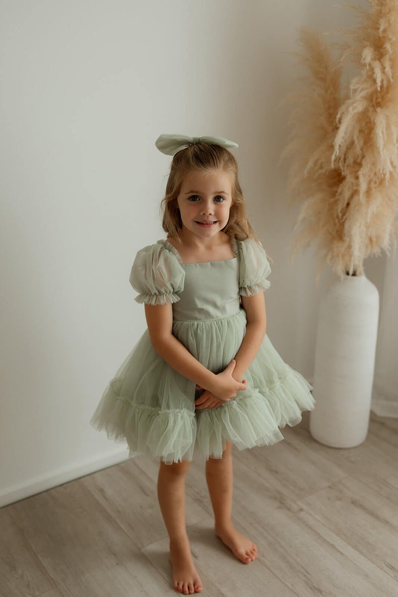 Sage green tulle Gabrielle flower girl dress with tulle puff sleeves is worn by a young girl.