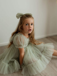 Gabrielle sage green flower girl dress is worn by a young girl. She also wears a matching sage green tulle bow in her hair.