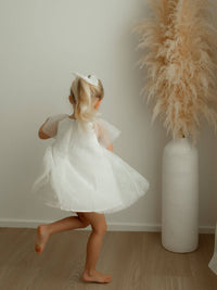 A little girl dances wearing our Gia baby flower girl romper in ivory.