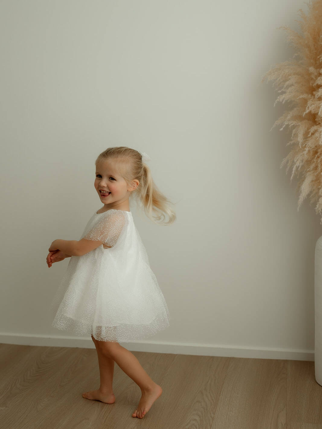 A little girl smiles wearing our Gia ivory baby flower girl dress.
