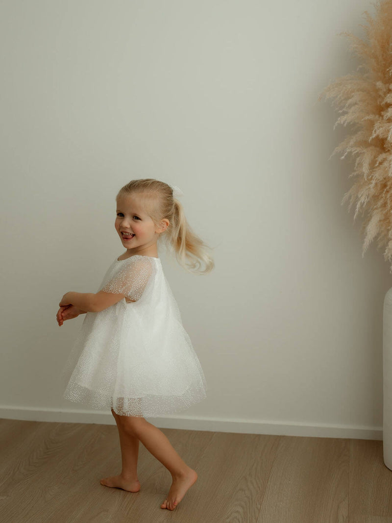 A little girl smiles wearing our Gia ivory baby flower girl dress.