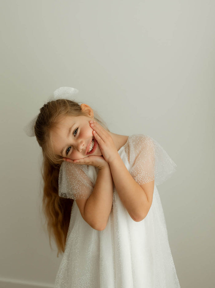 Young girl in a confetti tulle flower girl dress, our Gia dress and matching bow.