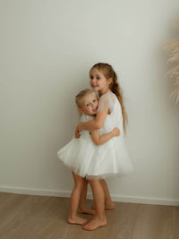 Sisters hug wearing matching ivory flower girl outfits.
