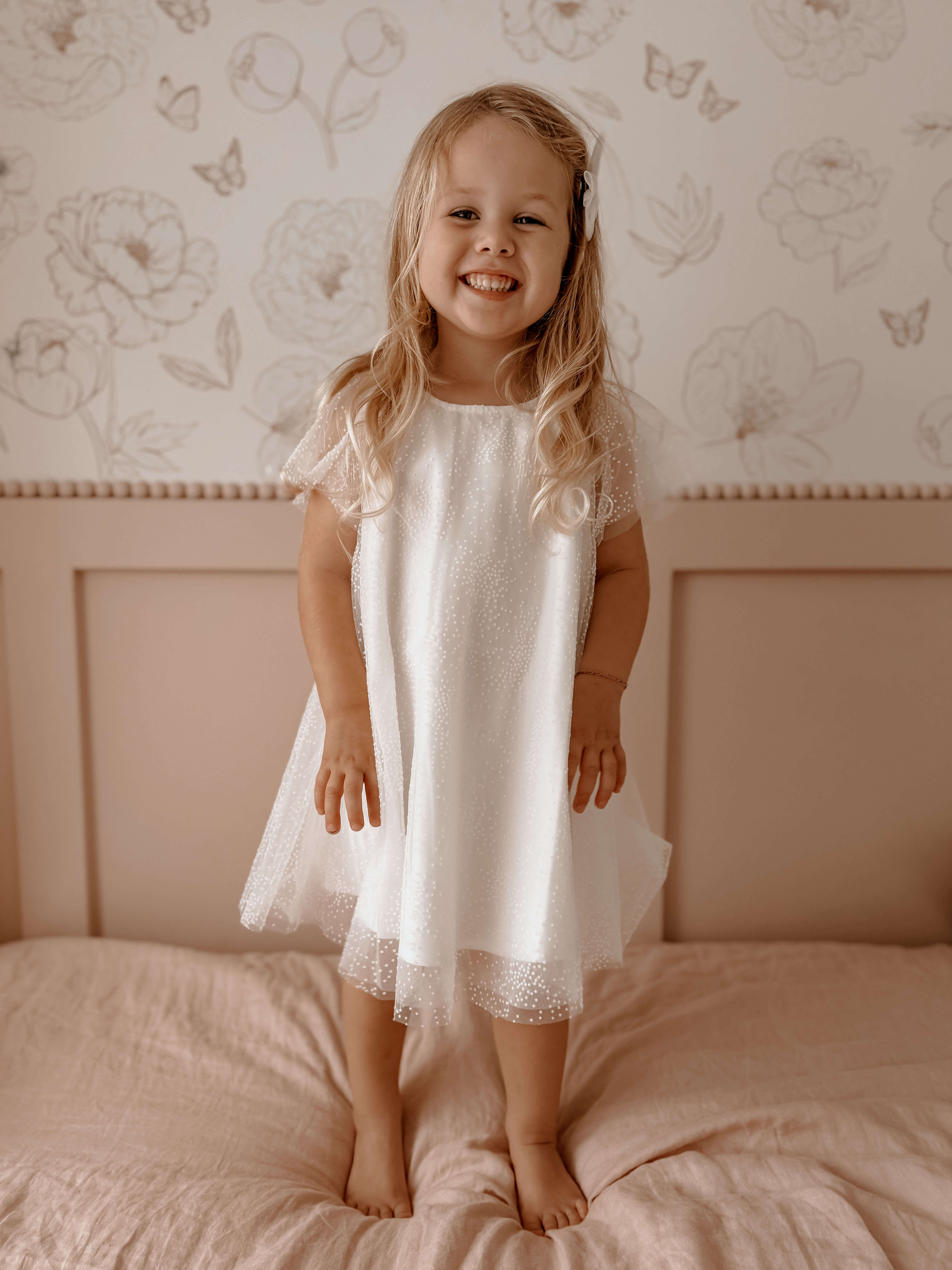 Gia flower girl dress in flocked dot tulle is worn by a young girl who is smiling.