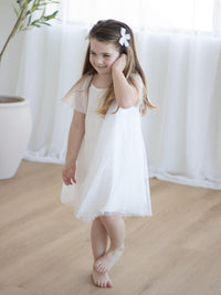 Young girl in our Gia flower girl dress standing on a wooden floor with a white curtain background.