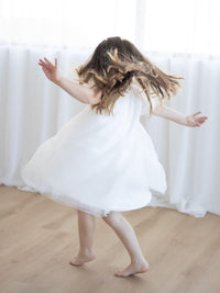 Child in our Gia flower girl dress dancing in front of white curtains.