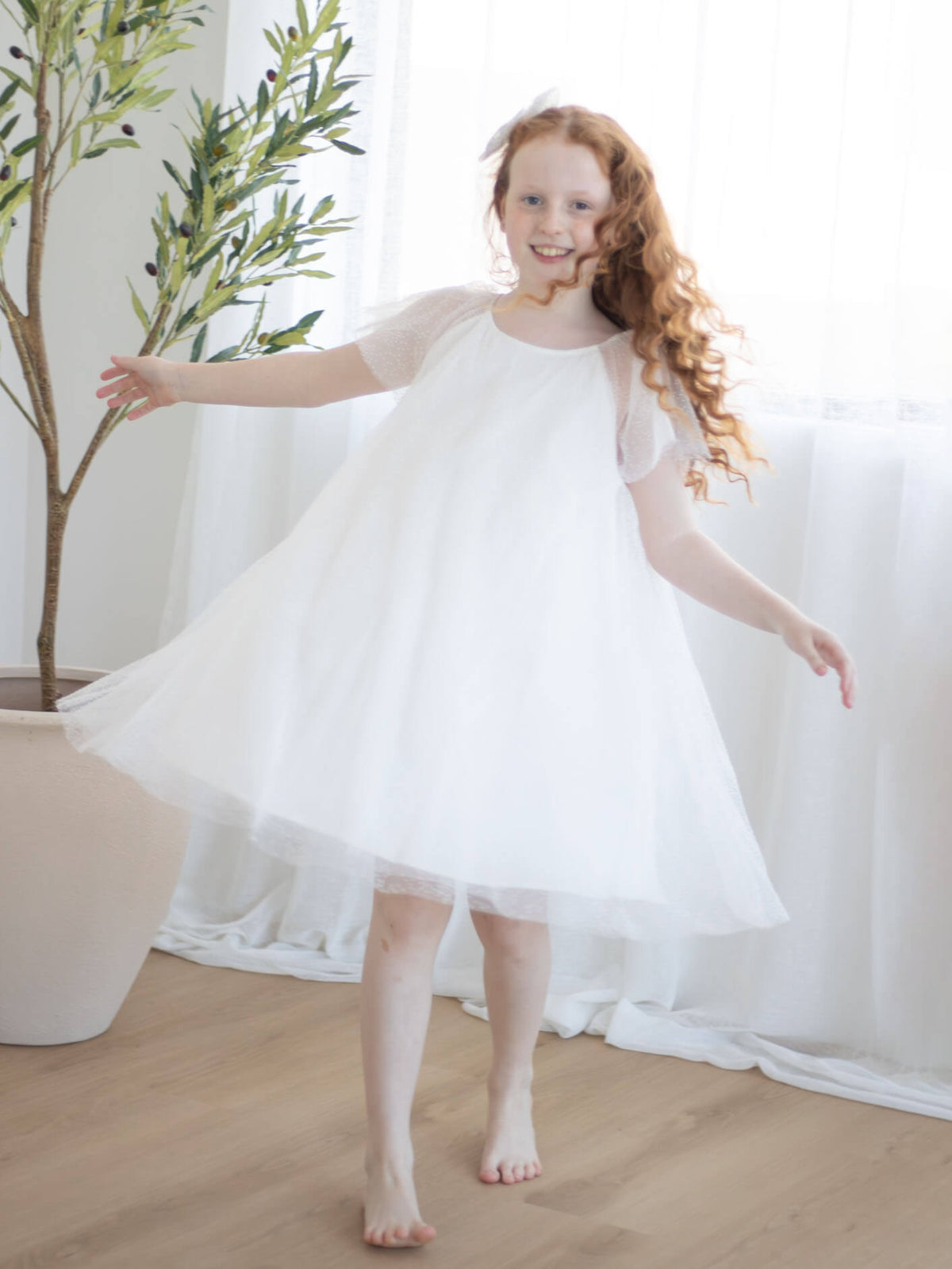 Young girl in our Gia flower girl dress standing indoors with a plant in the background.