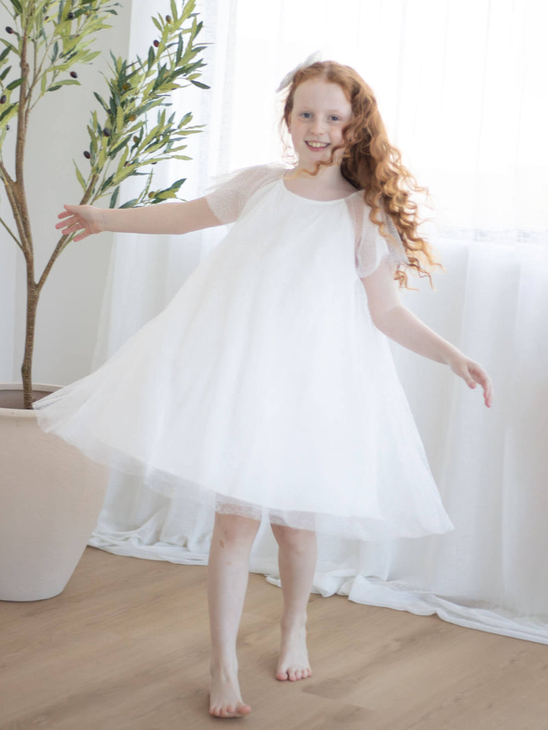 Young girl in our Gia flower girl dress standing indoors with a plant in the background.