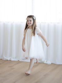 A little girl walks, smiling, wearing our Gia flower girl dress and matching small tulle bows.