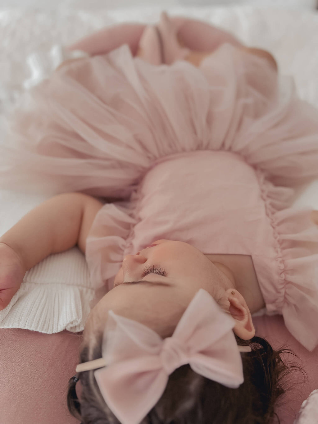 Baby girl sleeps wearing Gigi dusty pink baby flower girl dress and tulle bow headband.