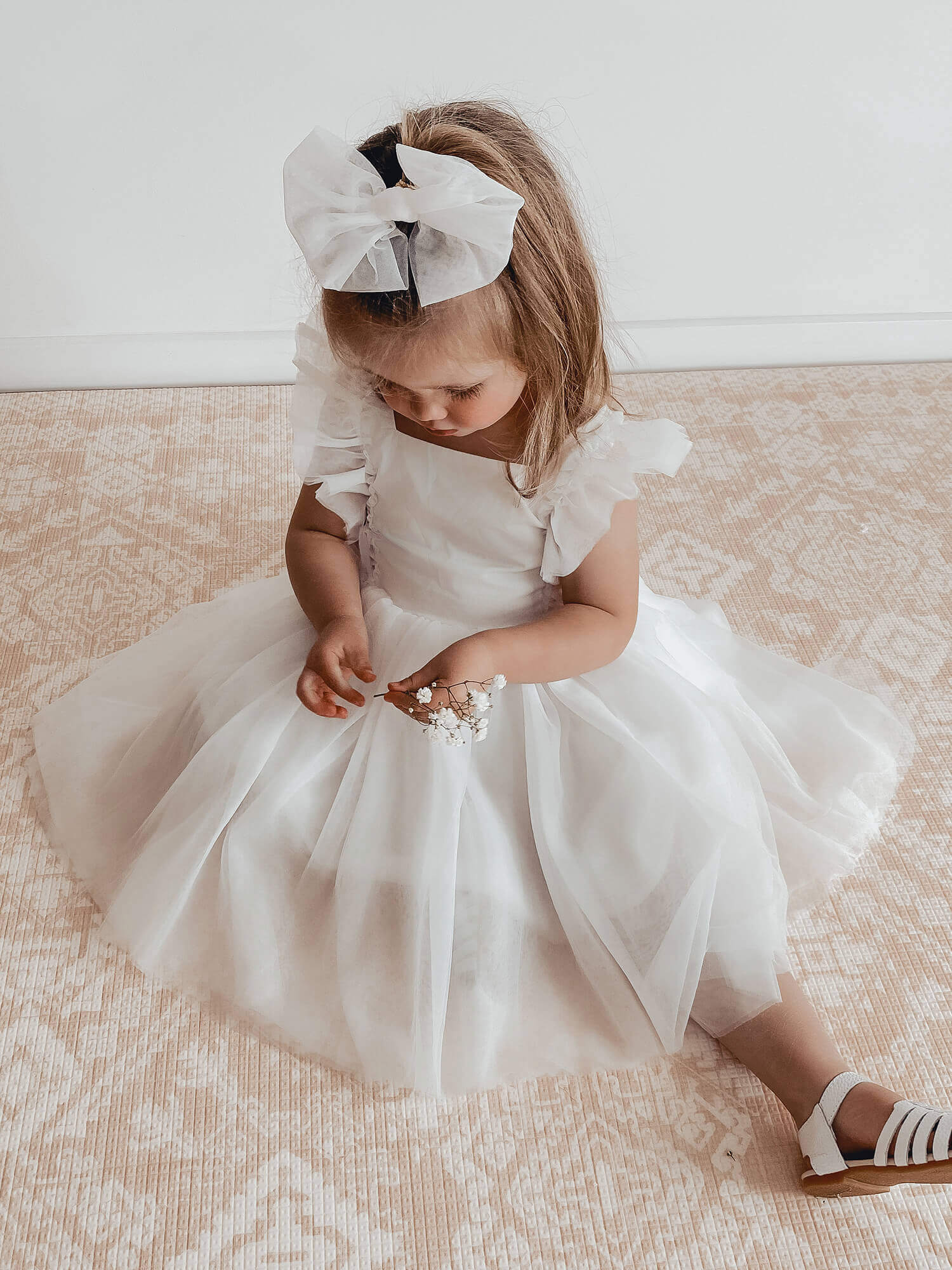 A young girl wears our Gigi ivory flower girl dress and our tulle bow in her hair.
