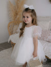 Gracie beaded puff sleeve flower girl dress in ivory is worn by a young girl. She also wears our medium tulle bow in her hair.