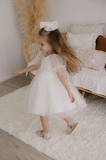 A young girl twirls wearing our Gracie flower girl dress and tulle bow hair clip.