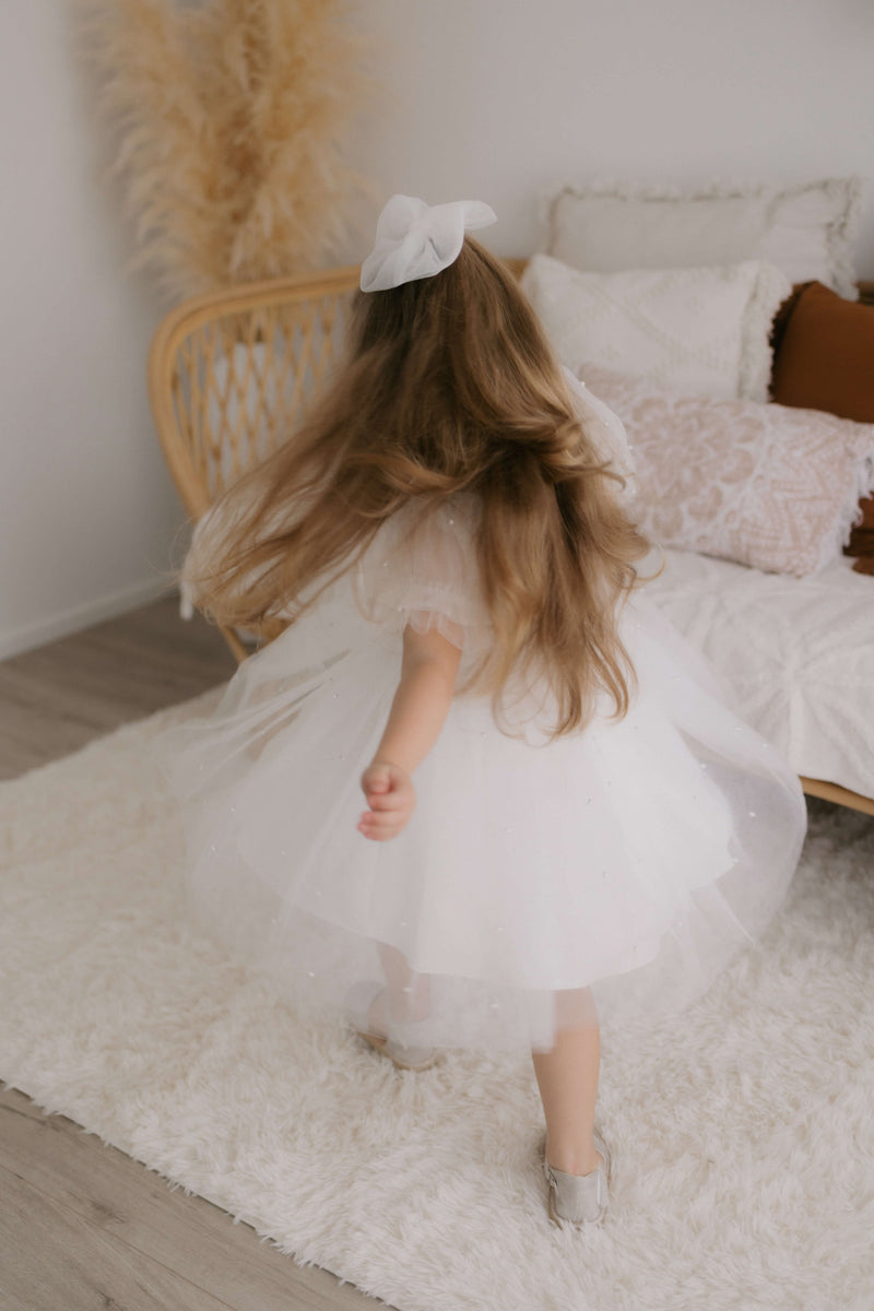 Twirling flower girl wears our Gracie beaded flower girl dress in ivory and ivory tulle bow hair clip.