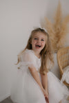 Laughing flower girl wears our Gracie tulle puff sleeve flower girl dress with beading, and tulle bow hair clip.