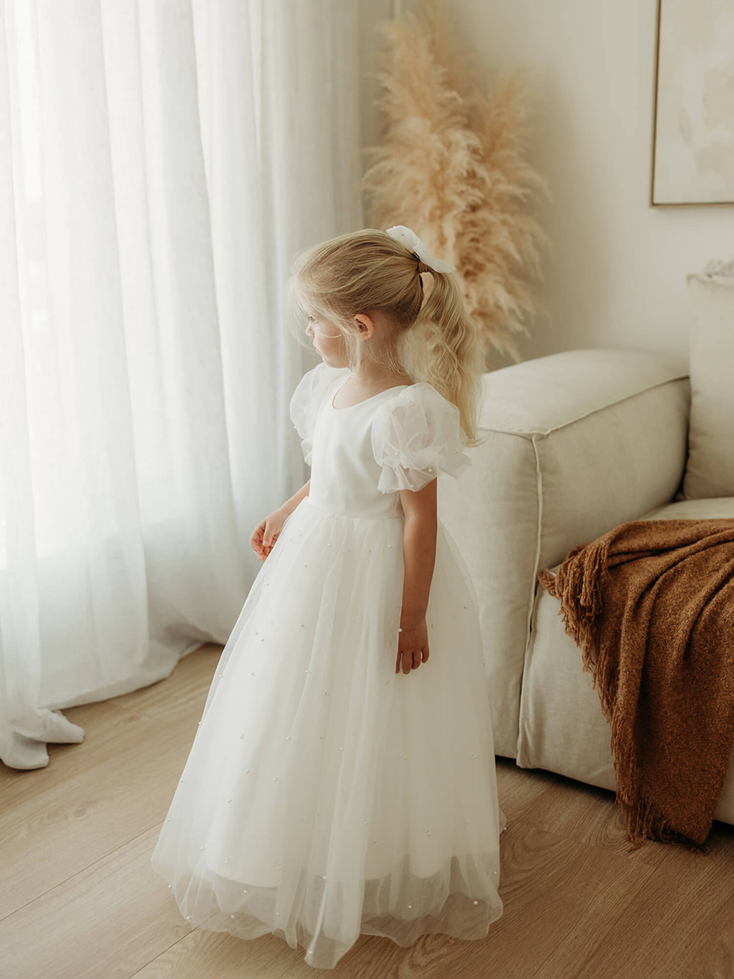 Gracie full length pearl flower girl dress is worn by a young girl. She also wears a matching tulle bow in her hair.
