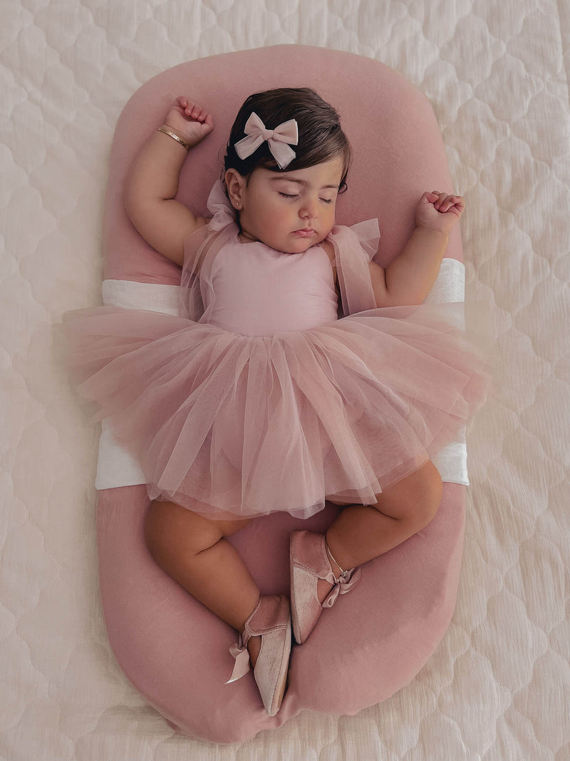 Baby girl sleeps wearing our dusty pink Harper baby flower girl romper and matching tulle bow hair clip.