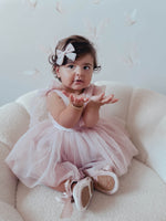 Harper dusty pink baby flower girl romper with tulle tie sleeves, worn by a baby. She also wears a matching tulle bow in her hair.