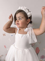 A toddler wears our Harper ivory baby flower girl romper dress, with soft tulle tie straps.