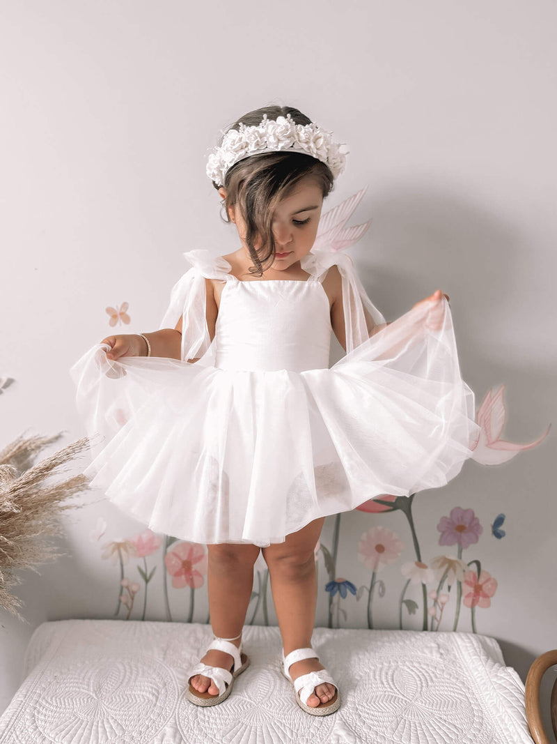A toddler stands wearing our Harper baby flower girl romper in light ivory.