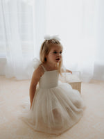 A young girl holds a basket and sits on the floor wearing our Harper flower girl dress.