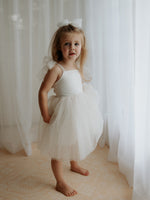 Full length photo of our Harper tea length flower girl dress in cream, worn by a young girl.